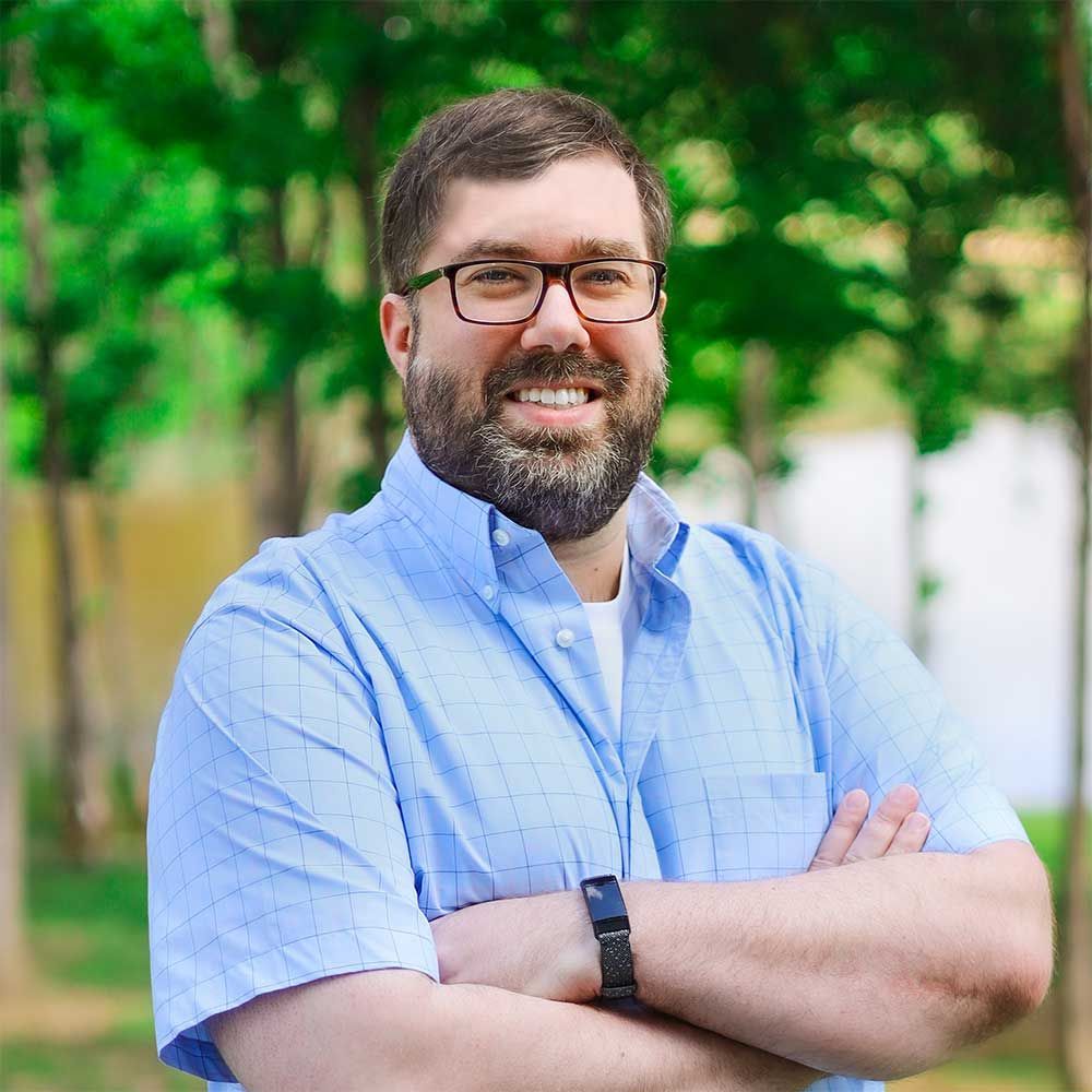 A man with a beard and glasses is smiling with his arms crossed.