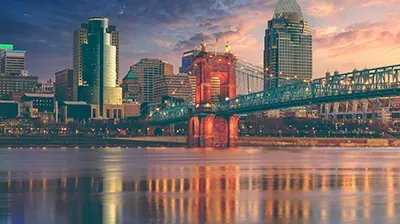 The Cincinnati skyline and the John A. Roebling Suspension Bridge over the Ohio River at sunset.