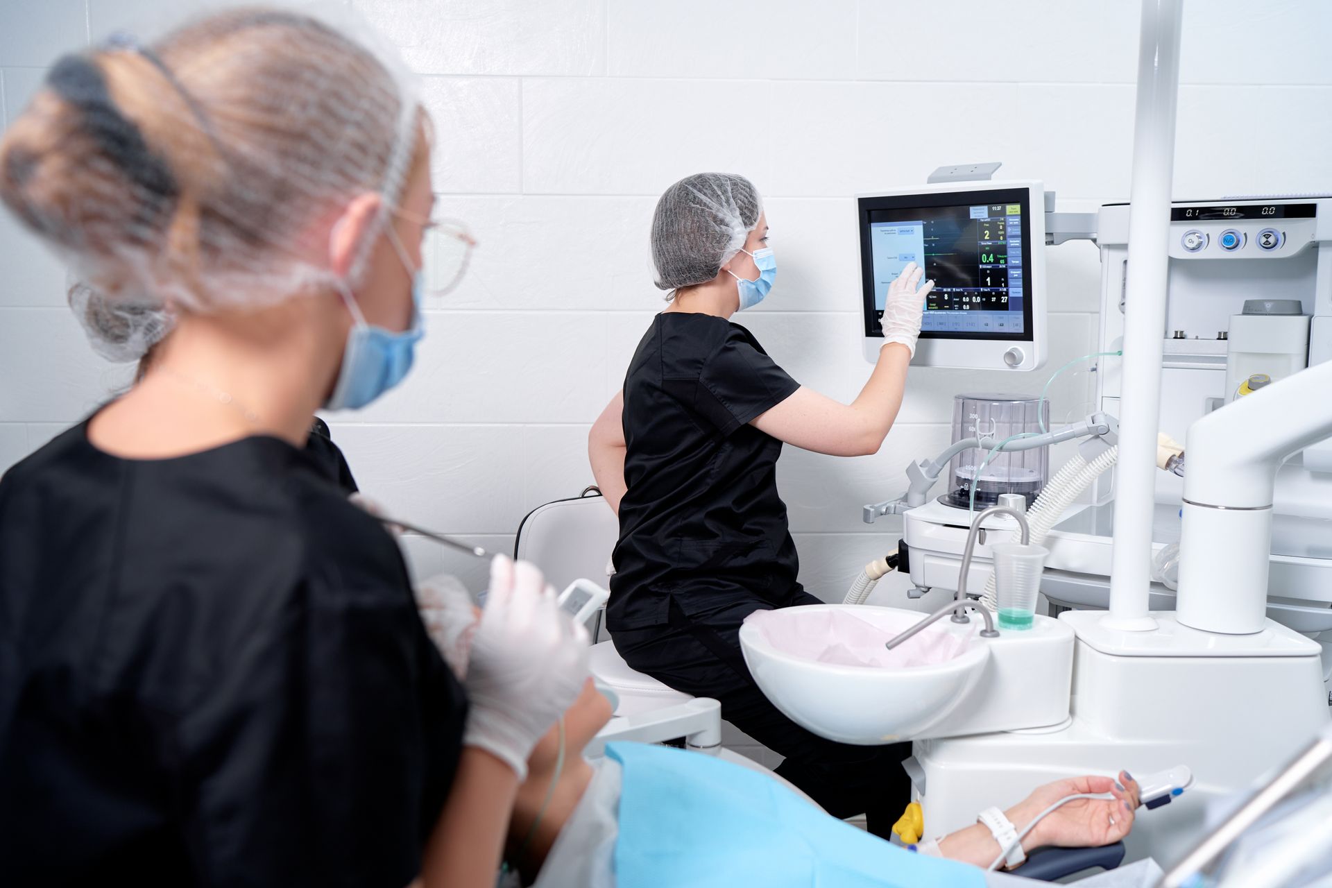 A doctor administers anaesthesia, and another is checking a monitor while a patient lies in a chair. A doctor administers anaesthesia, and another is checking a monitor while a patient lies in a chair.