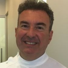 Man with gray hair, smiling, wearing a white collared shirt.