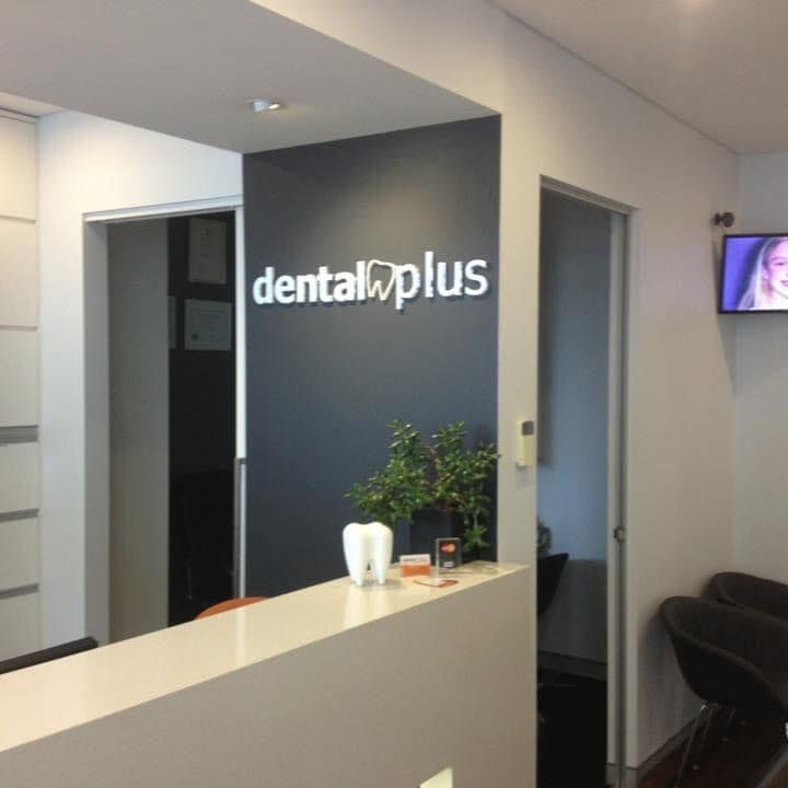 Reception area of Dental Plus with white counter, dark grey wall, and a small television.