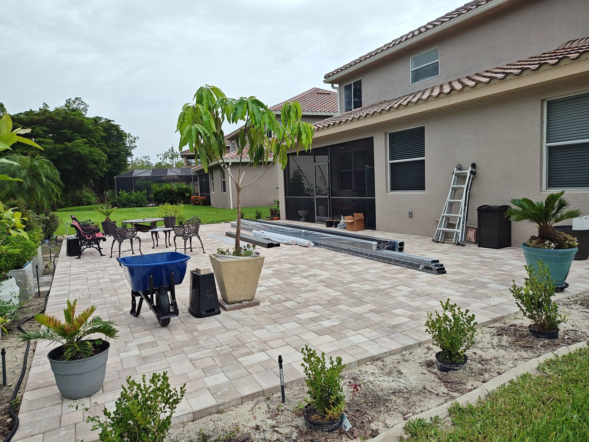 A patio with a wheelbarrow and potted plants in front of a house.