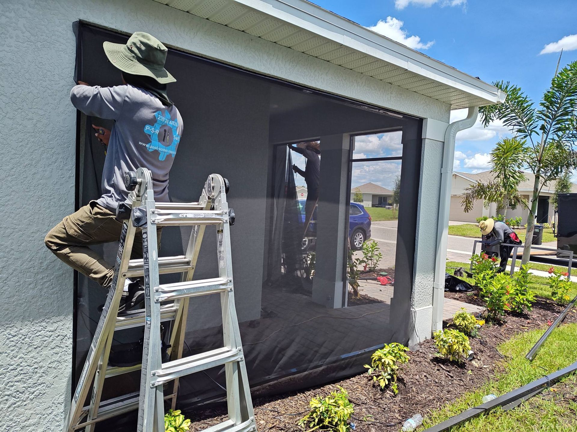 A man is standing on a ladder installing a screen door on a house.