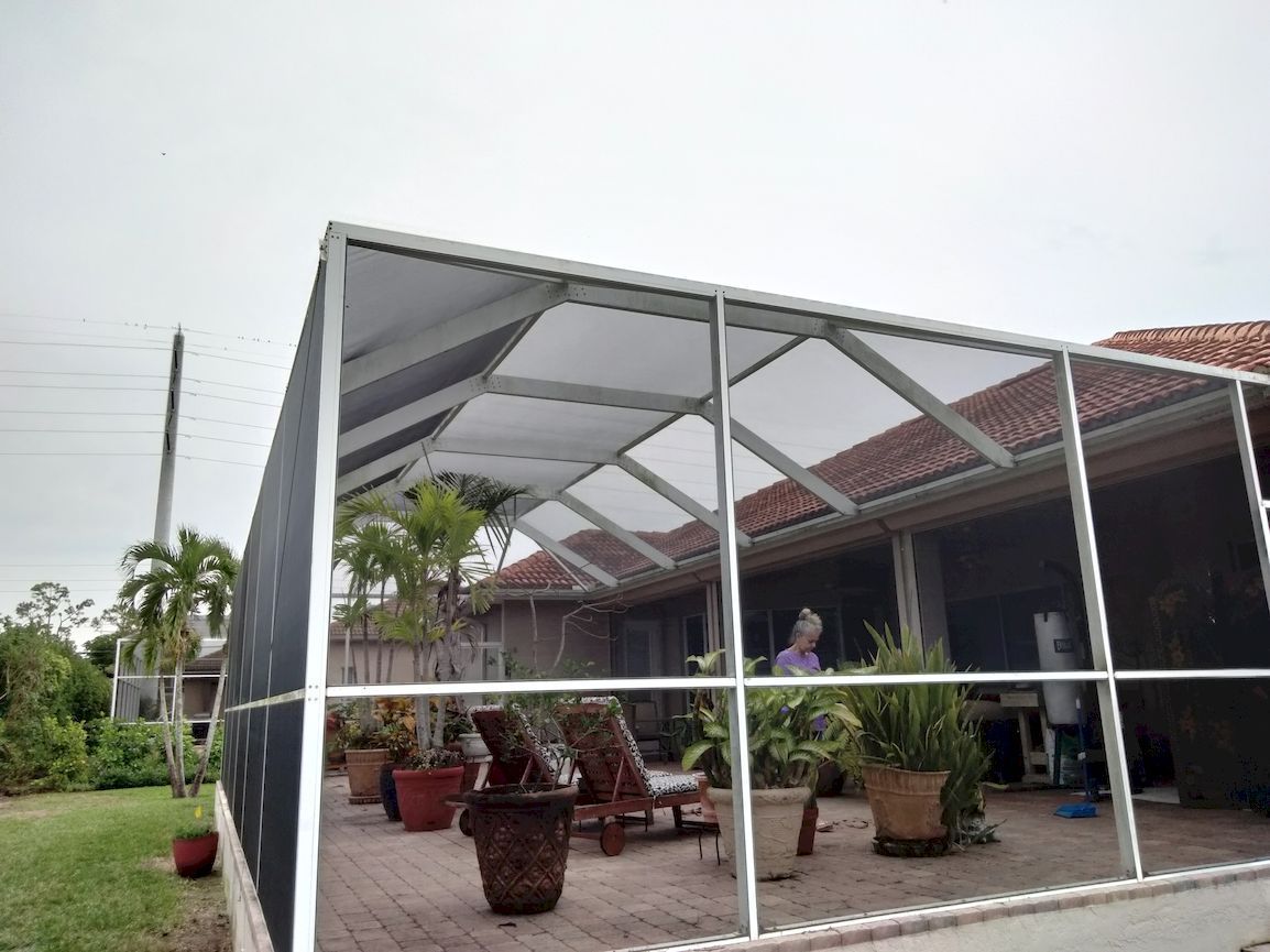 A screened in porch with chairs and potted plants in front of a house.