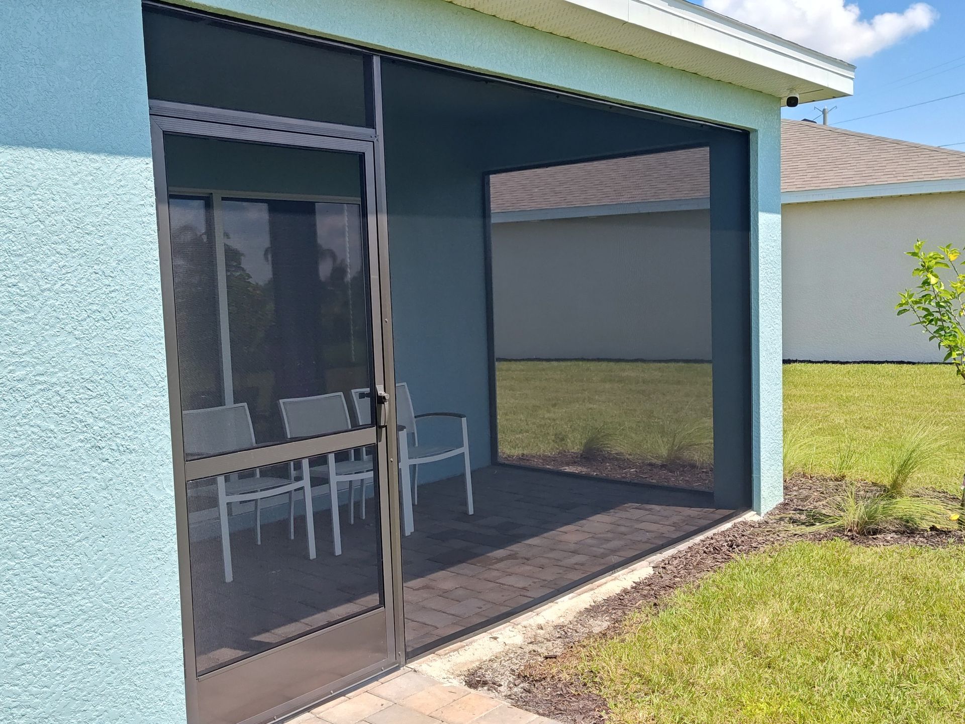 A screened in porch with a table and chairs in the backyard of a house.