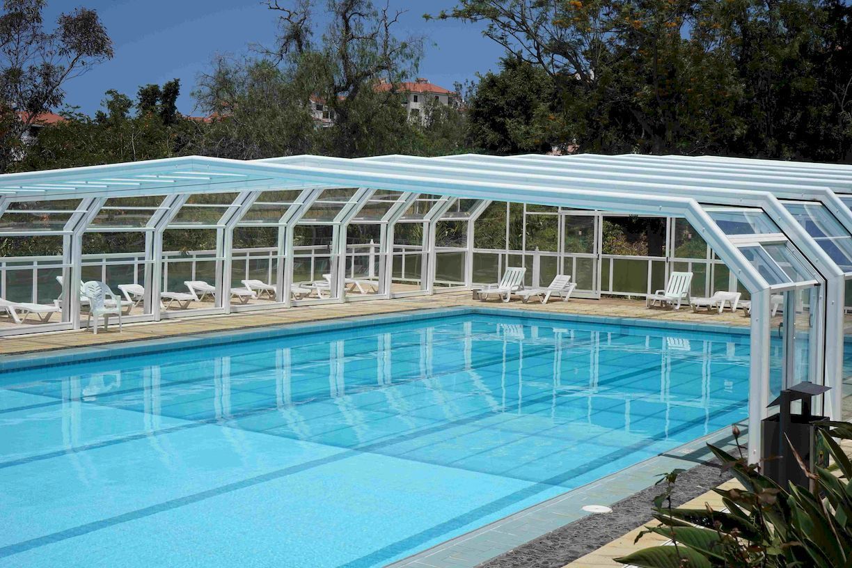 A large swimming pool with a clear roof and chairs around it.