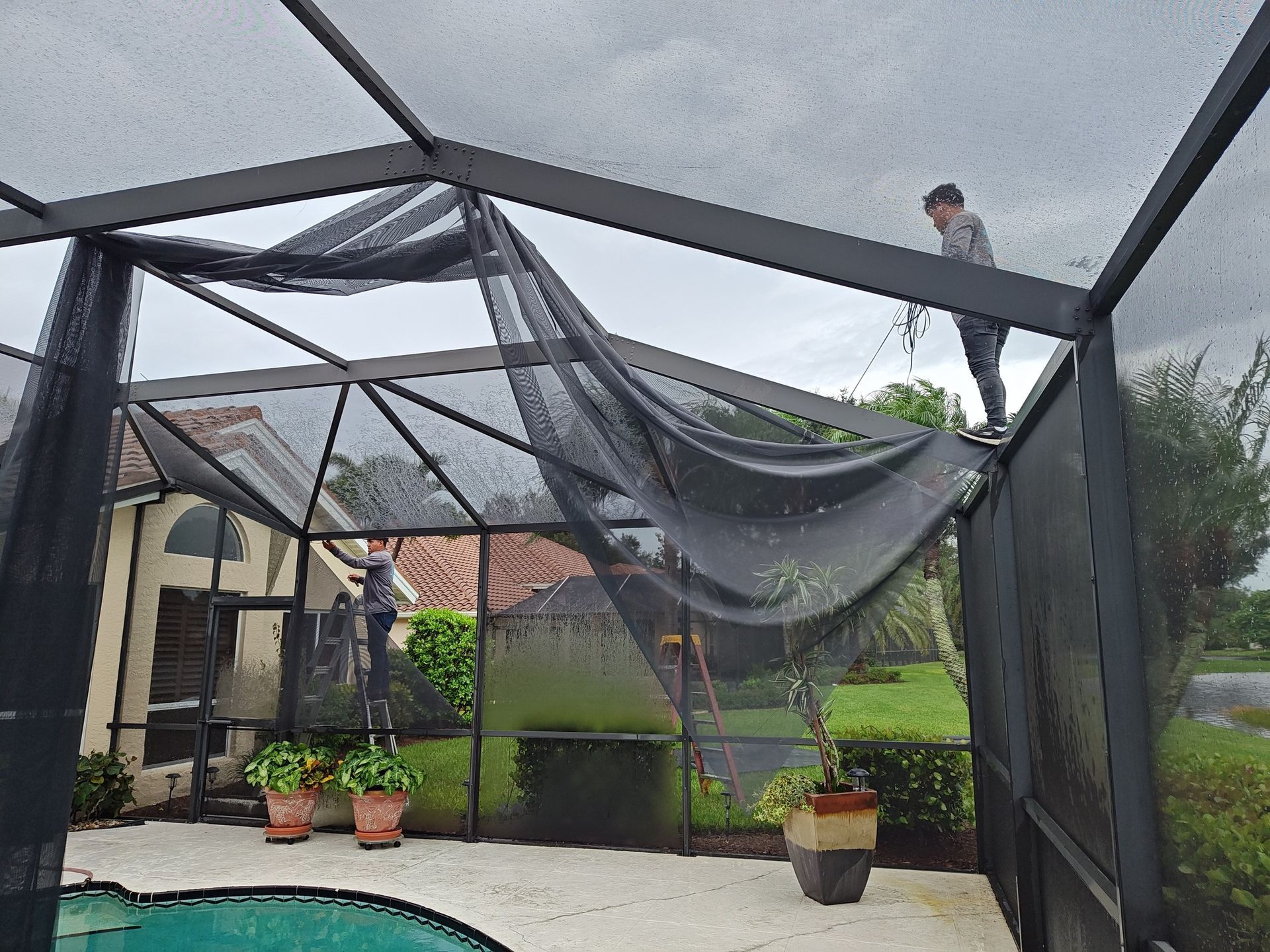 A man is standing on top of a screened in area next to a pool.