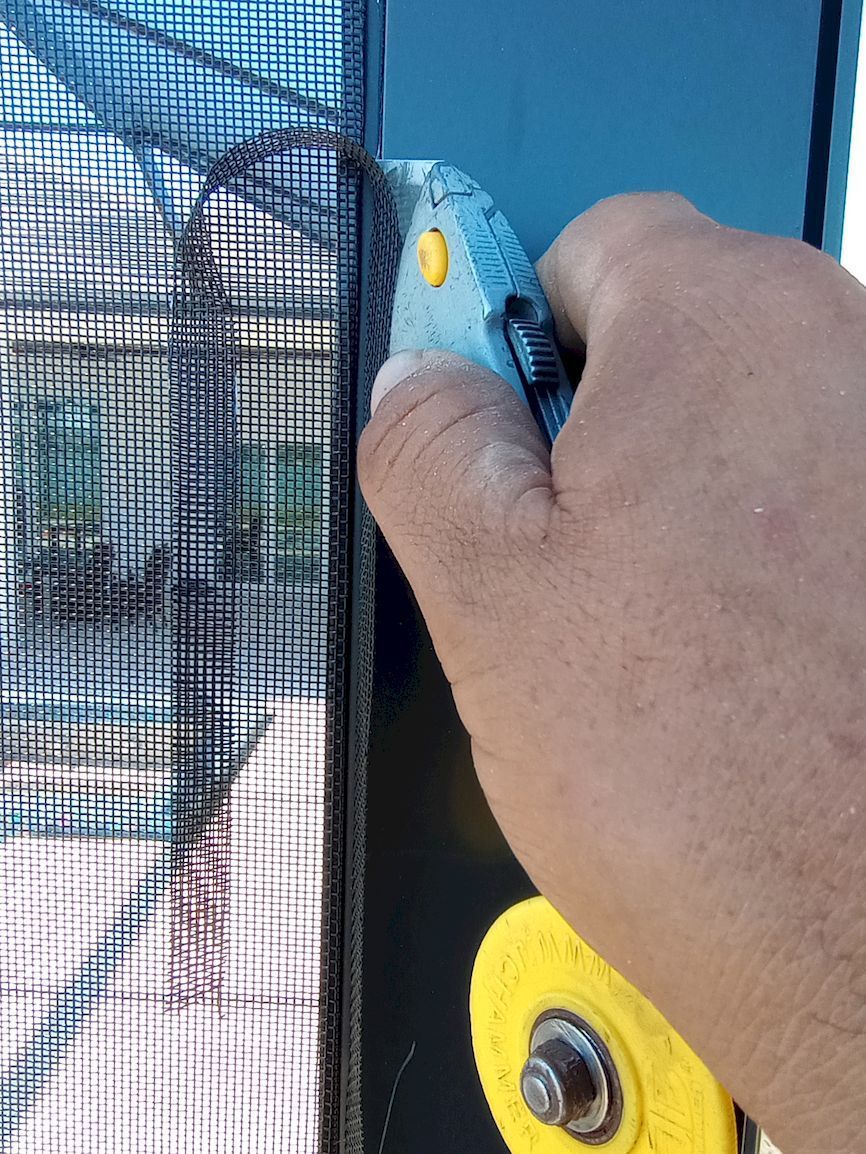 A close up of a person cutting a screen door with a pair of scissors