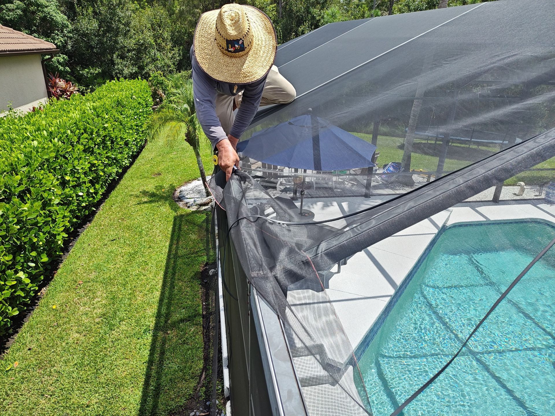 A man wearing a straw hat is working on a pool fence.
