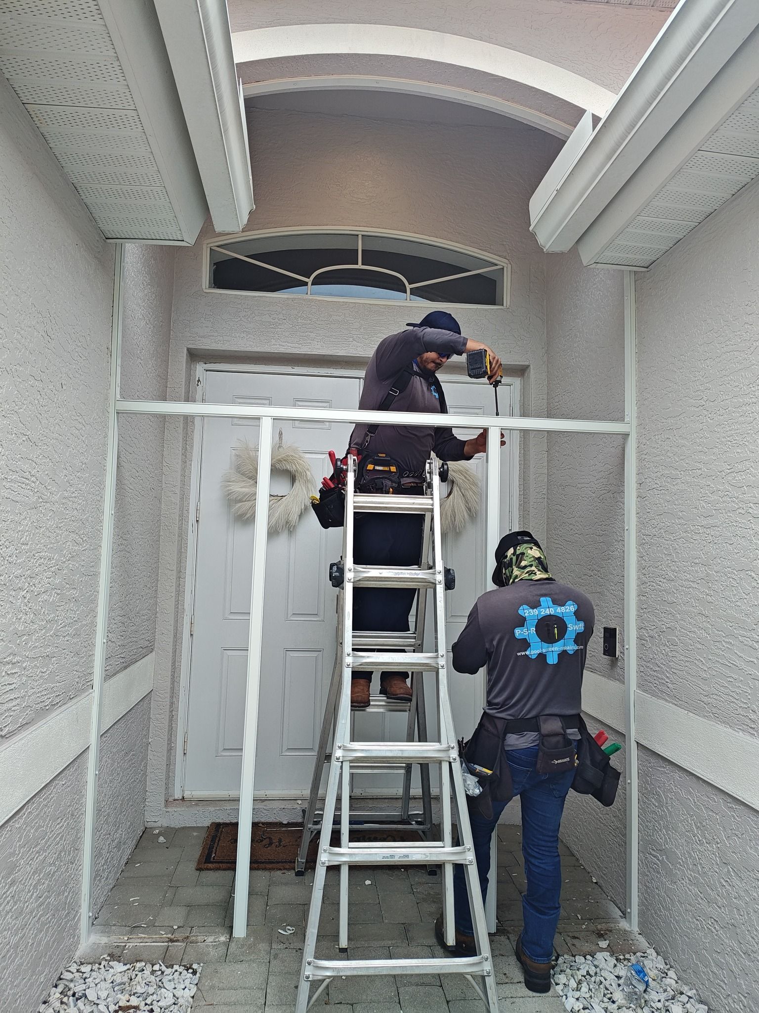 Two men are standing on a ladder working on a door.