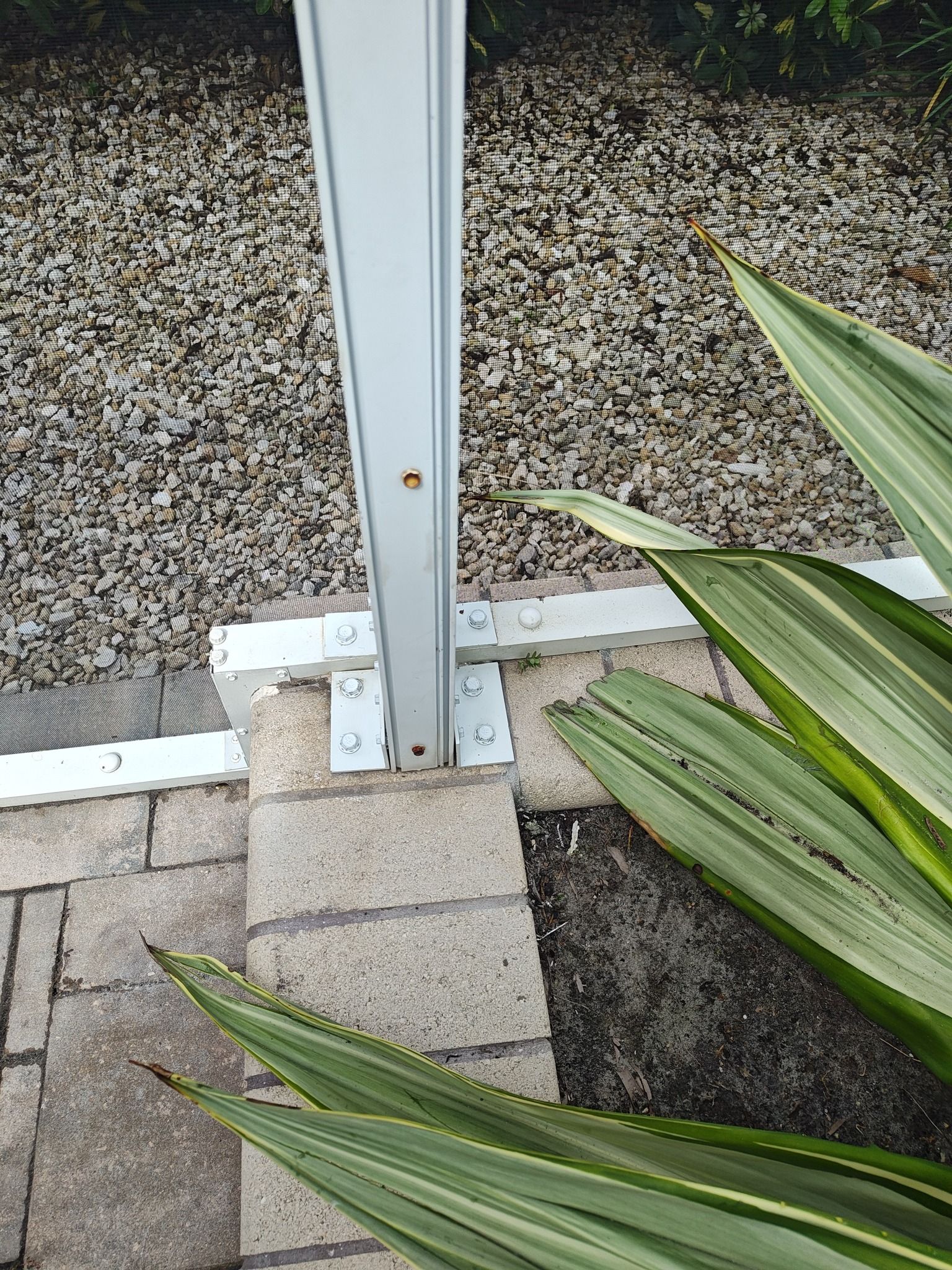 A white pole is sitting on top of a brick walkway next to a plant.