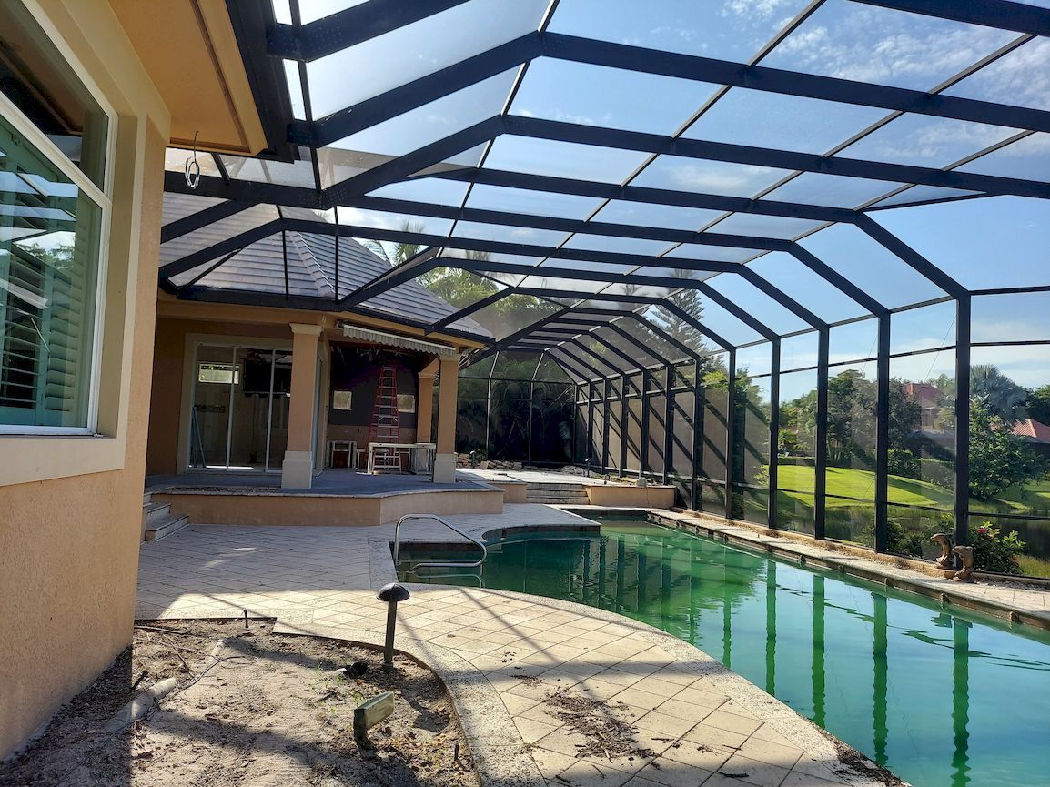 There is a swimming pool in the backyard of a house with a screened in area.