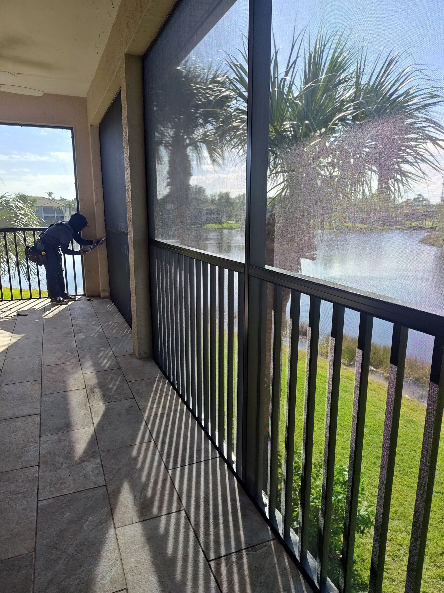 A screened in porch with a view of a lake and palm trees.