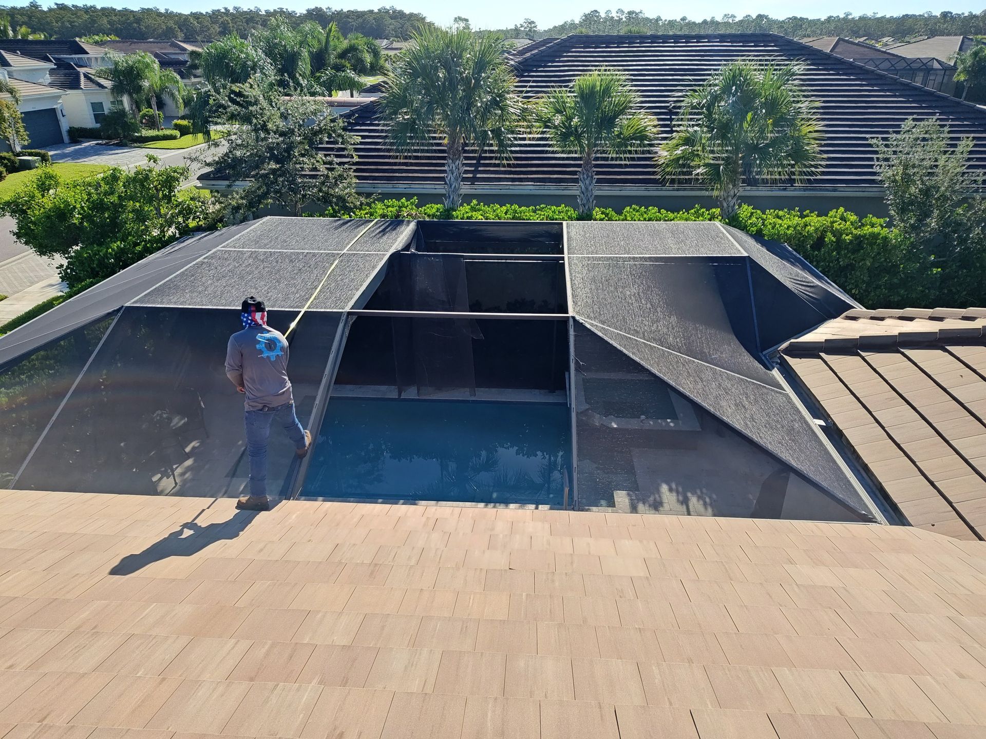A man is standing on the roof of a house next to a swimming pool.