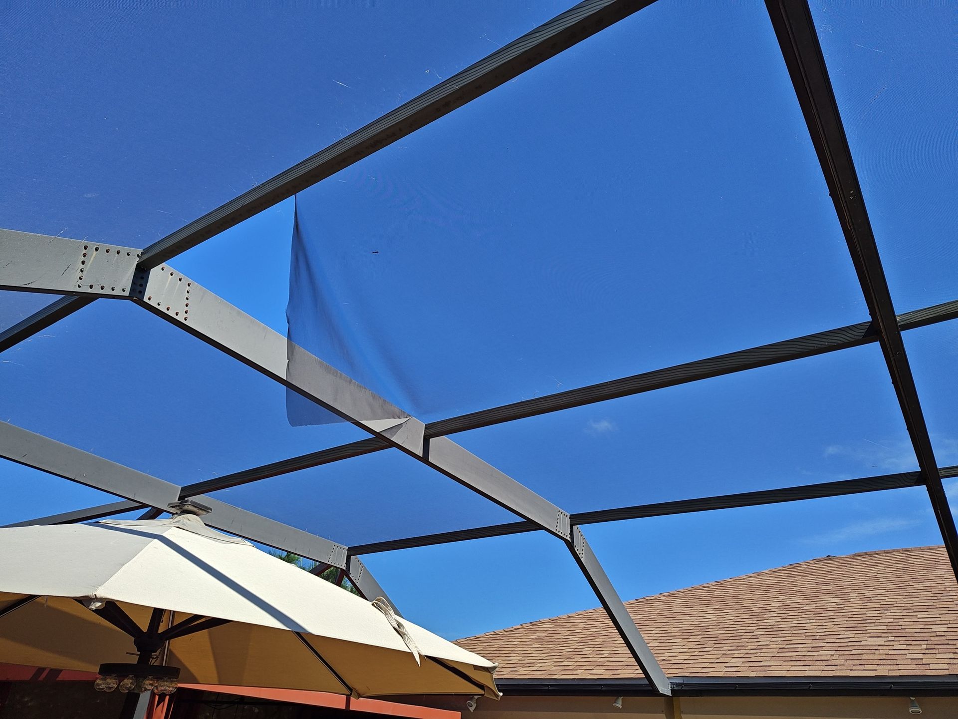 A white umbrella is under a clear roof with a blue sky in the background