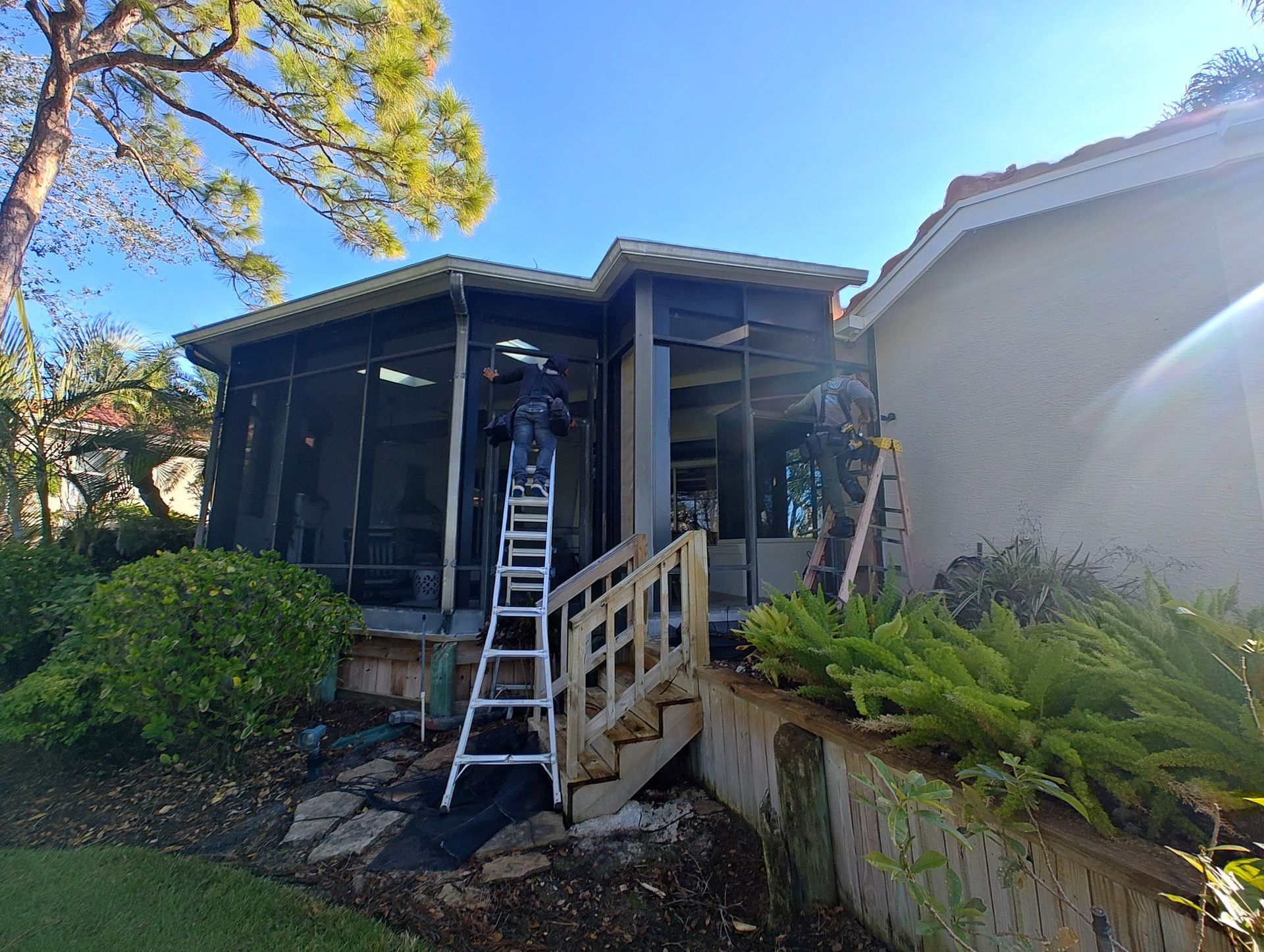 A man is standing on a ladder in front of a screened in porch.