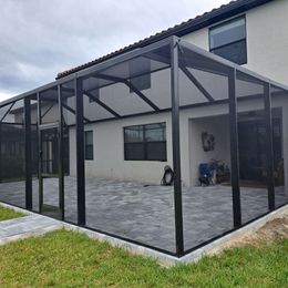 A screened in porch with a patio in front of a house.