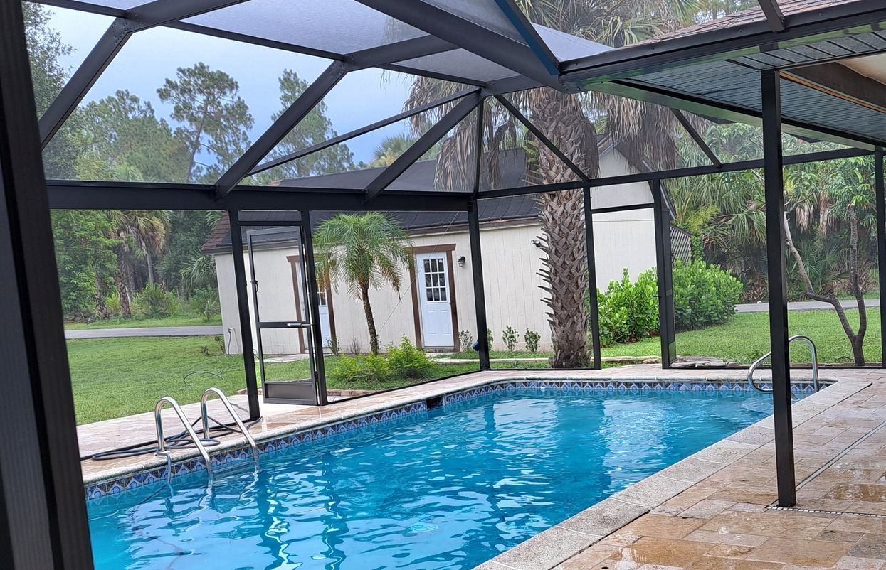 A large swimming pool is covered by a screened in area.