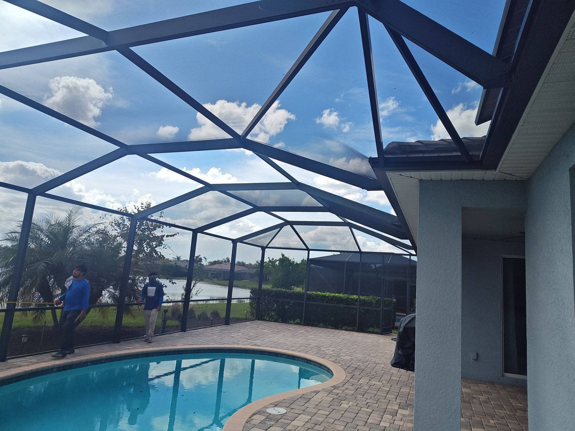 A man is standing next to a swimming pool under a screened in area.