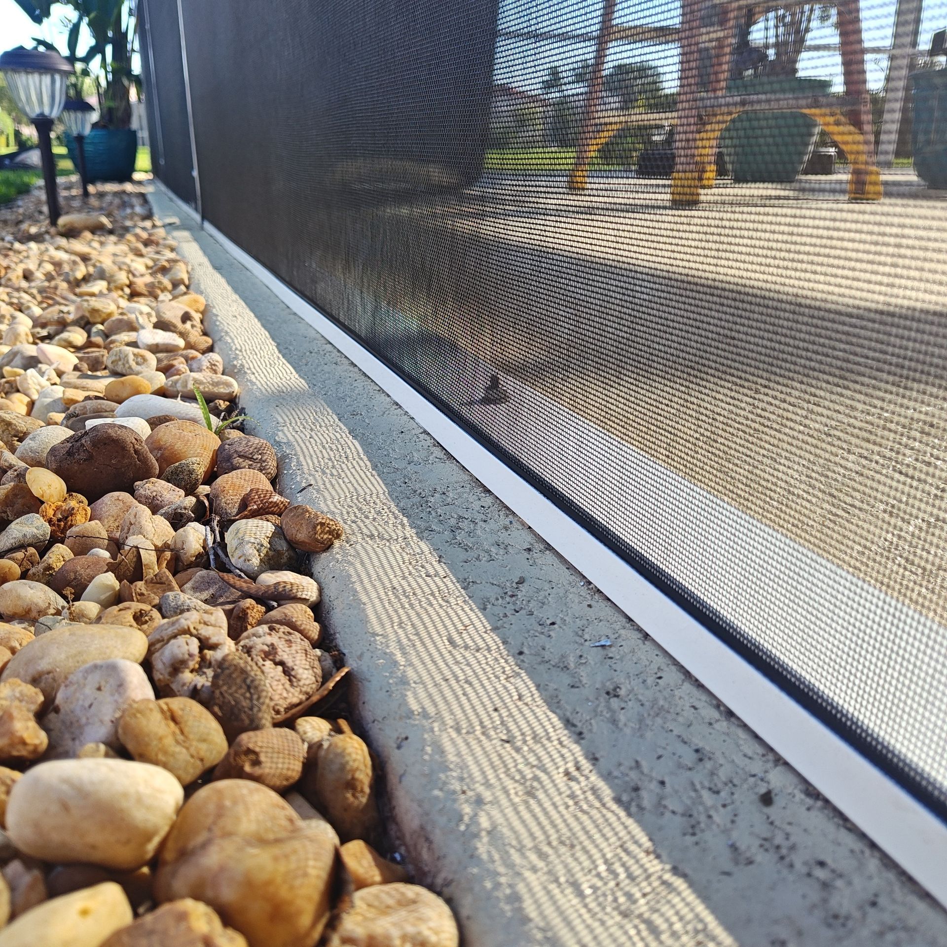 A fence with a screen on it is surrounded by rocks.