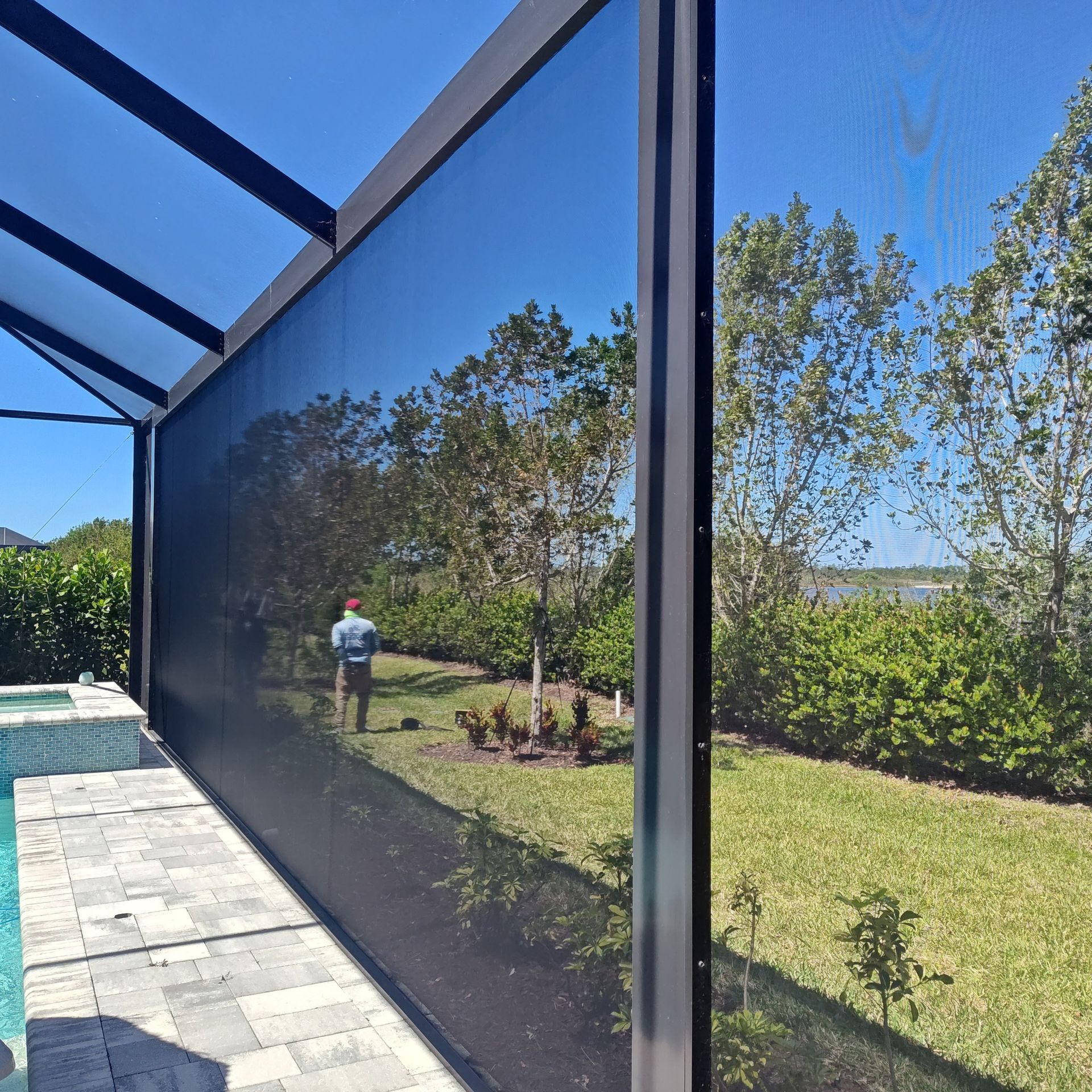 A man is standing in front of a screened in porch overlooking a swimming pool