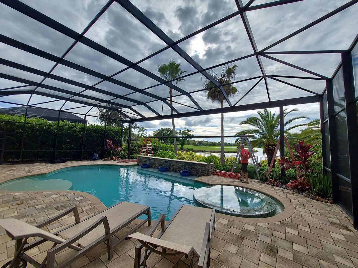 A man is standing in front of a screened in swimming pool.