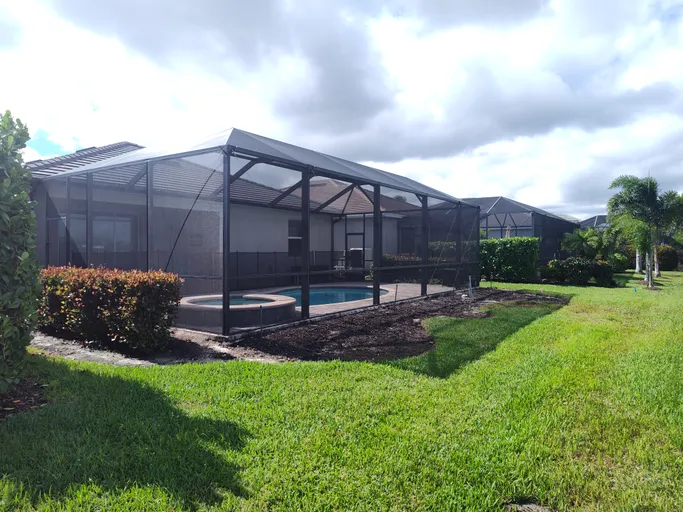 A screened in backyard with a pool and a hot tub.