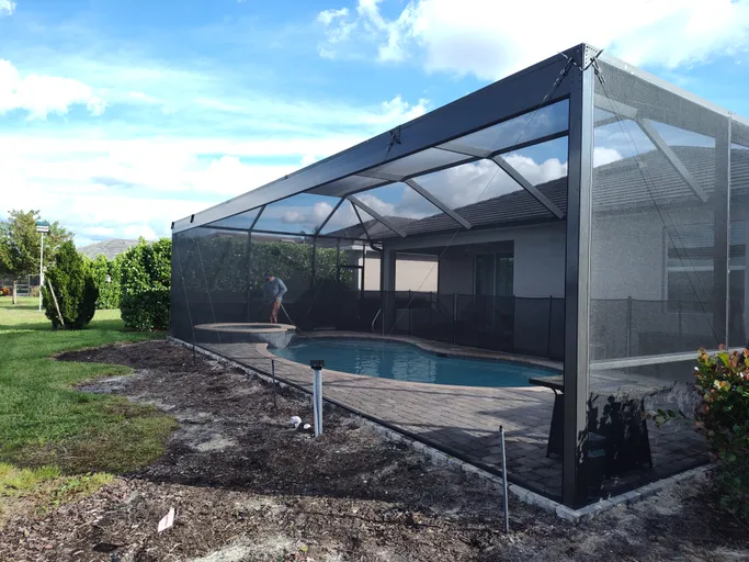 A screened in swimming pool in the backyard of a house.