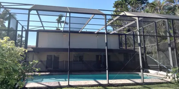 A house with a screened in pool in front of it.