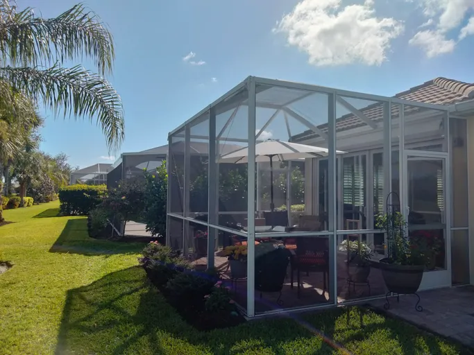 A screened in porch with a table and chairs and umbrellas in the backyard of a house.