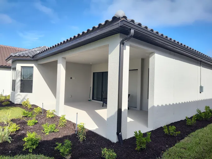 A white house with a porch and a gutter on the side of it.