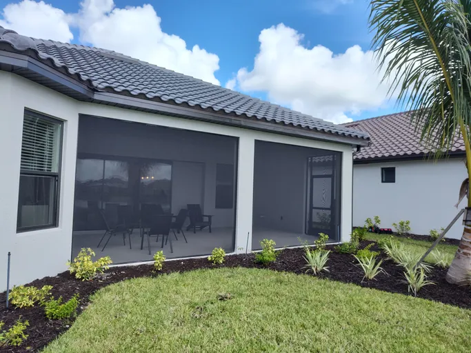 A white house with a screened in porch and a palm tree in front of it.
