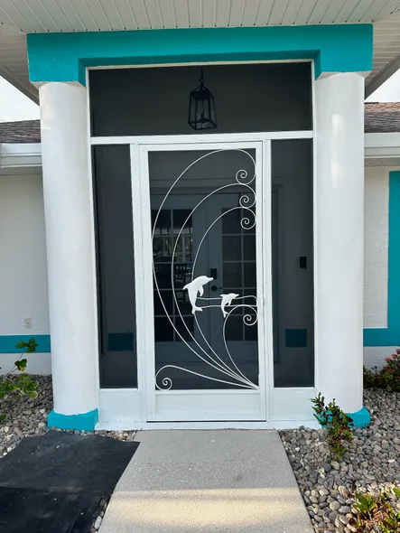 A white house with blue trim has a screen door with dolphins on it