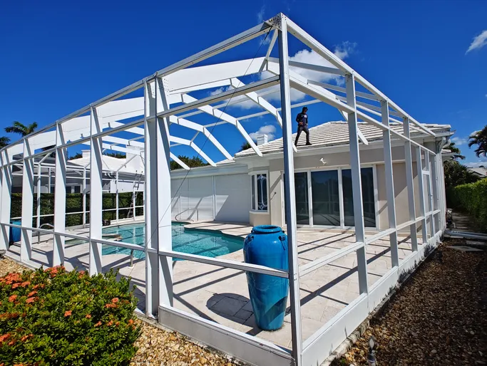 A man is standing on the roof of a house next to a swimming pool.