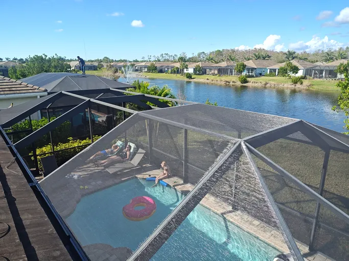 A man is standing on top of a screened in swimming pool.