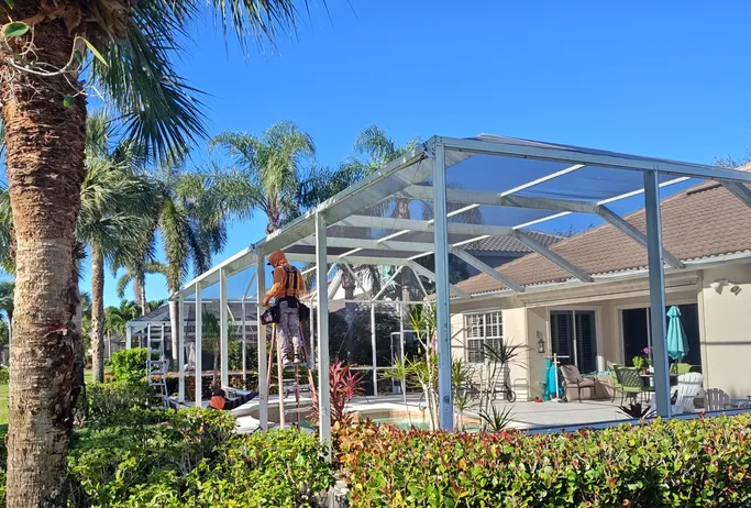A man is working on a screened in porch in front of a house.