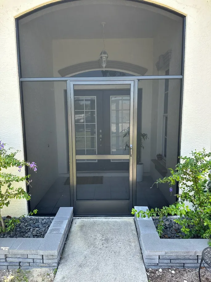 The front door of a house with a screen door and a walkway leading to it.