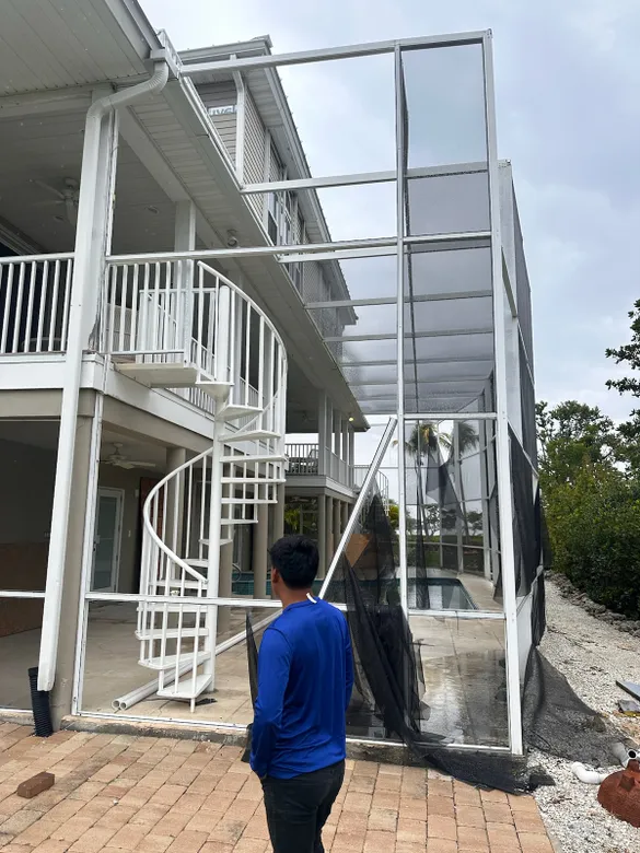 A man in a blue shirt is standing in front of a house with a spiral staircase.