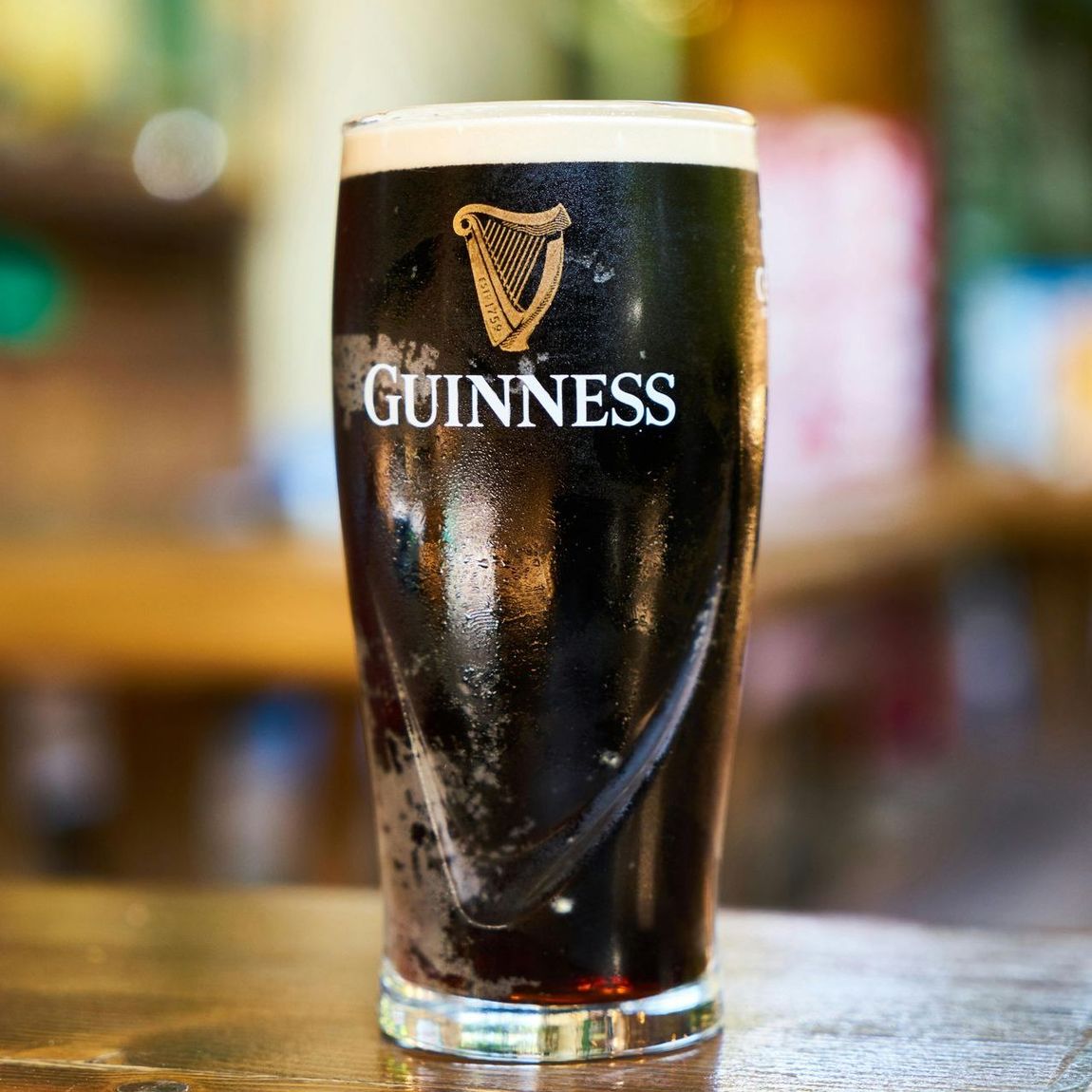 A glass of guinness beer is sitting on a wooden table.