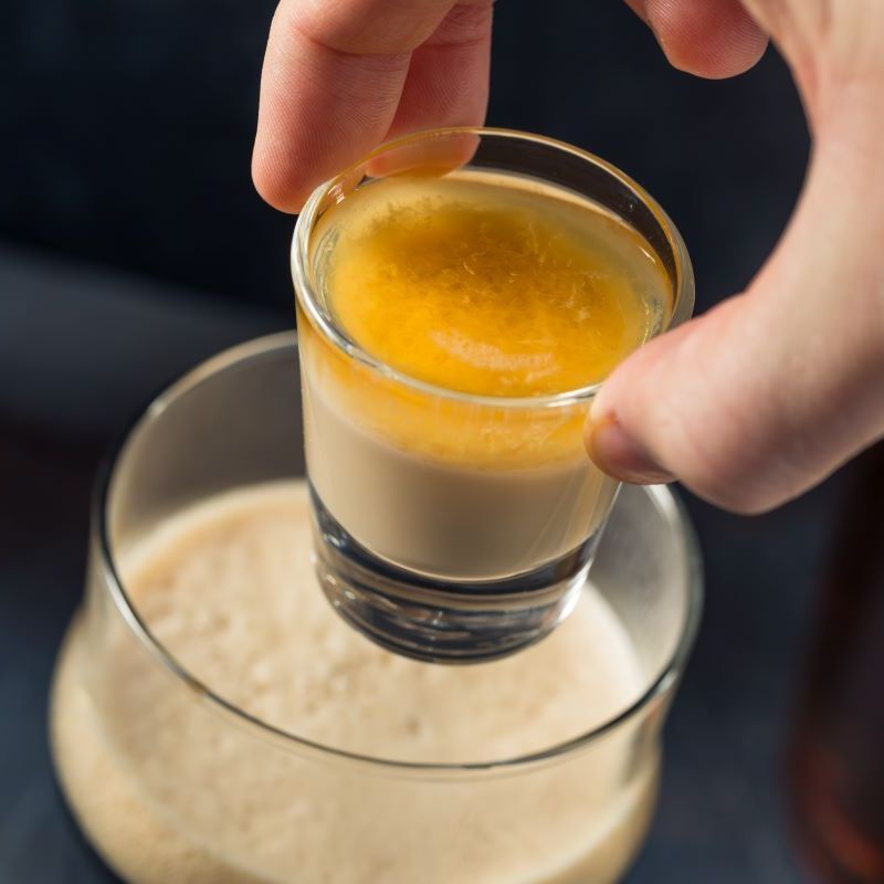 A person is pouring a shot of liquid into a glass of beer