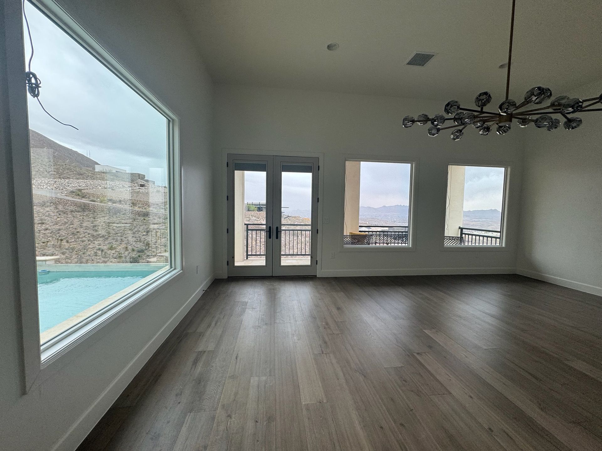 An empty living room with a large window and a swimming pool in the background.
