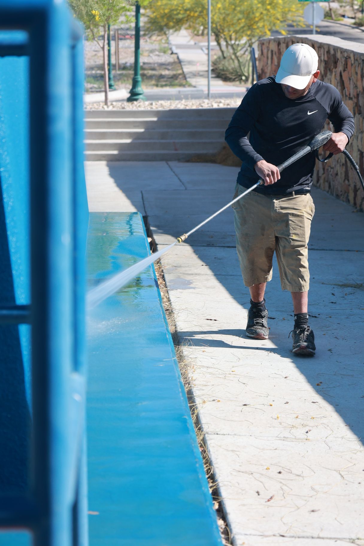 Person spraying water along a blue poolside walkway outdoors