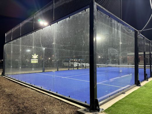 A tennis court with a clear fence around it at night.