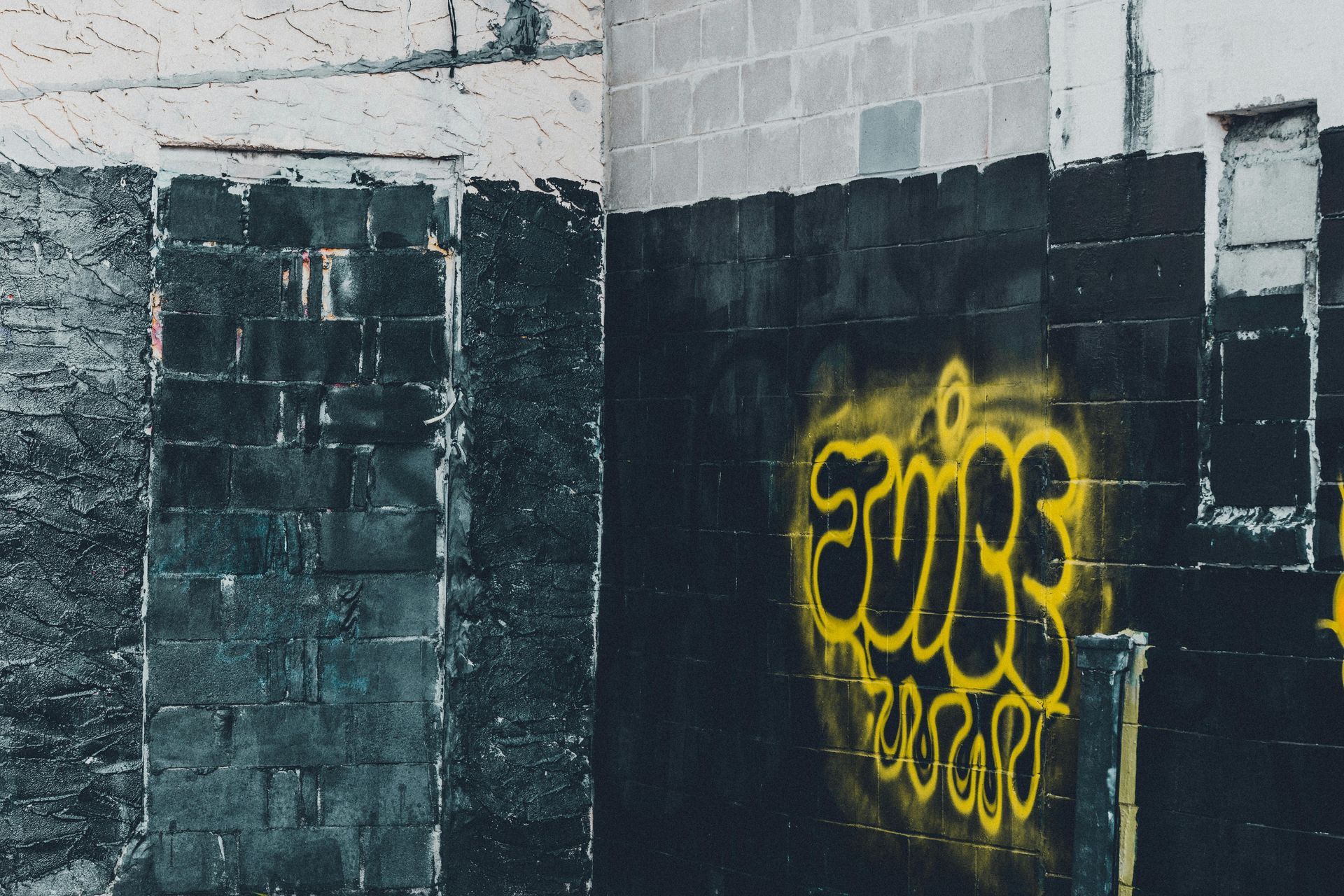 Yellow graffiti on a dark brick wall in an industrial alley