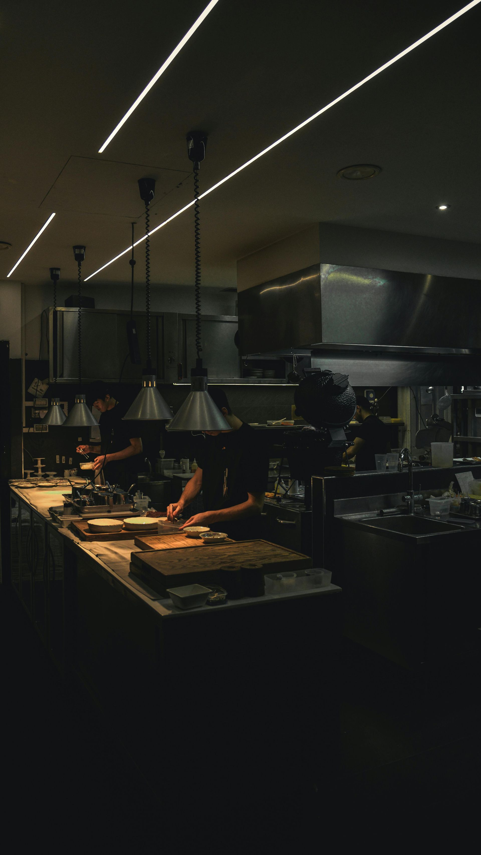 Dimly lit buffet counter with food trays, hanging lights, and a modern kitchen interior