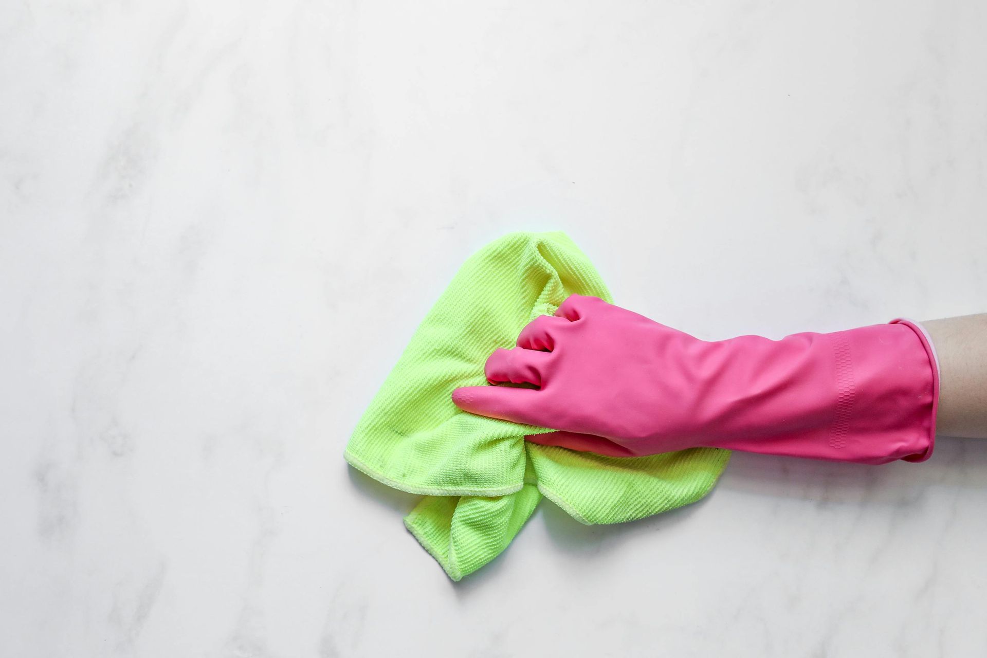 A gloved hand wiping a white surface with a green cloth.