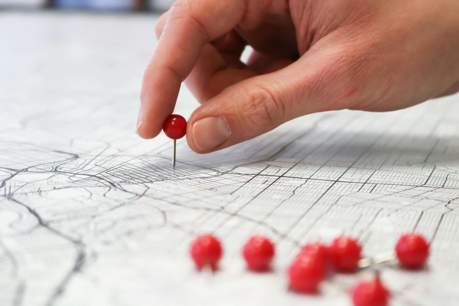 Hand placing a red push pin on a detailed map, with other pins scattered nearby.