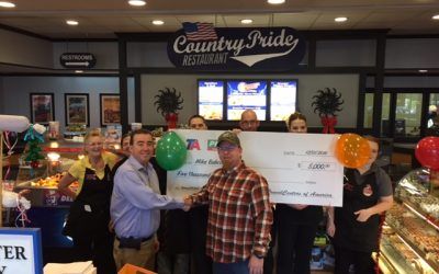 A group of people holding a large check in front of a country pride restaurant.