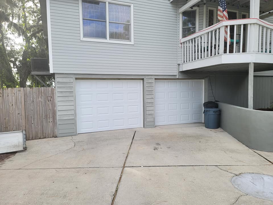 A white house with two garage doors and a balcony.
