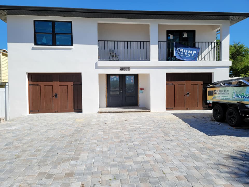 A white house with two garage doors and a truck parked in front of it.